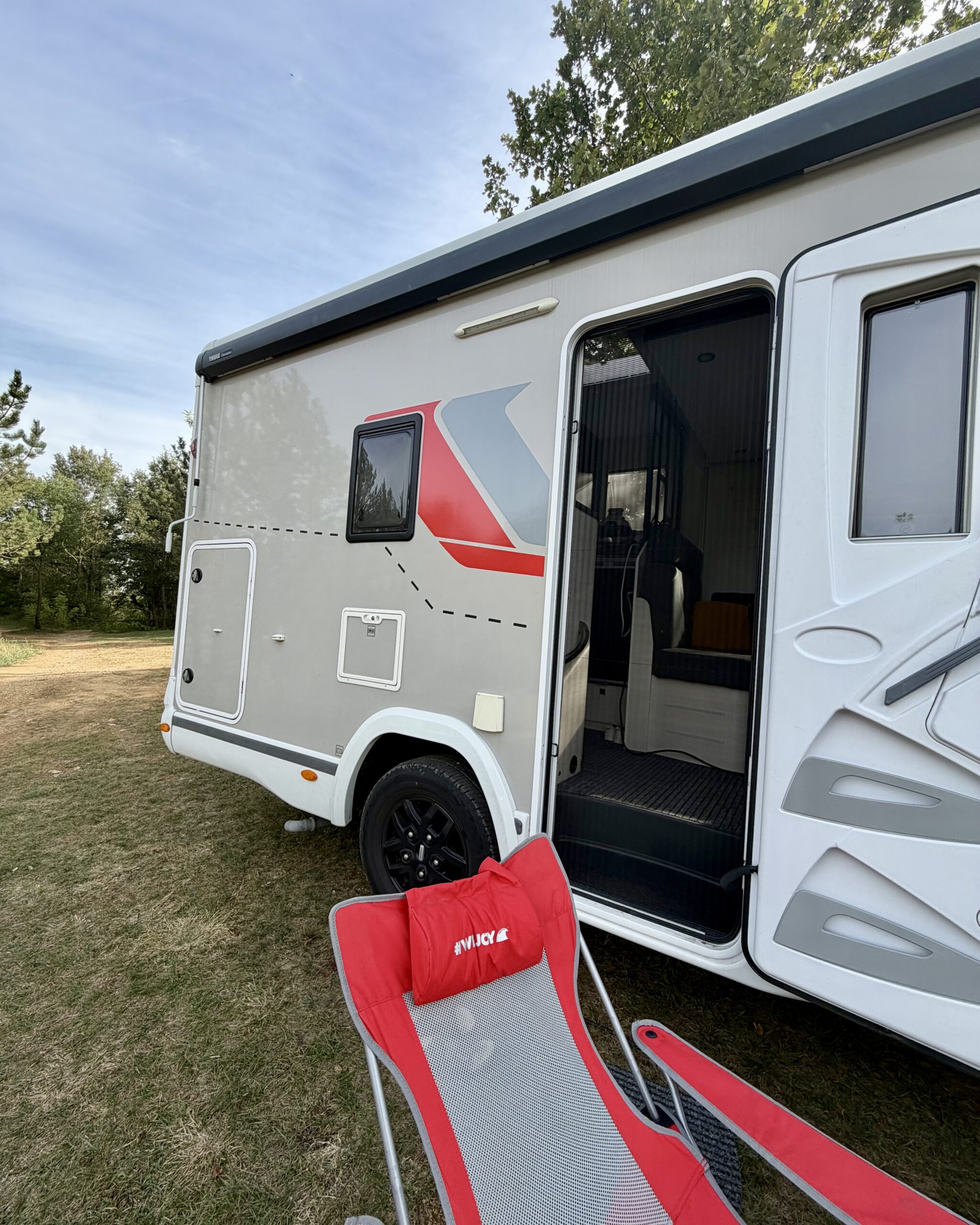 Wohnmobil mit geöffnetem Eingang und Campingstuhl auf einer Wiese bei Camping Peruca